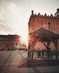 People walking in historic building against sky during sunset