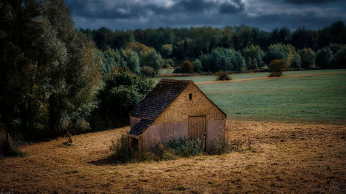 House on field by trees against sky