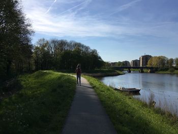 Rear view of woman walking on grass by trees against sky