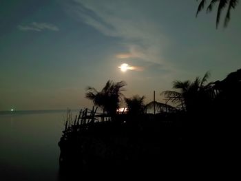 Silhouette palm trees by sea against sky during sunset