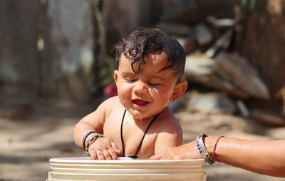 Photo of a small newborn indian baby taking a bath with a bucket full of water with unclothed