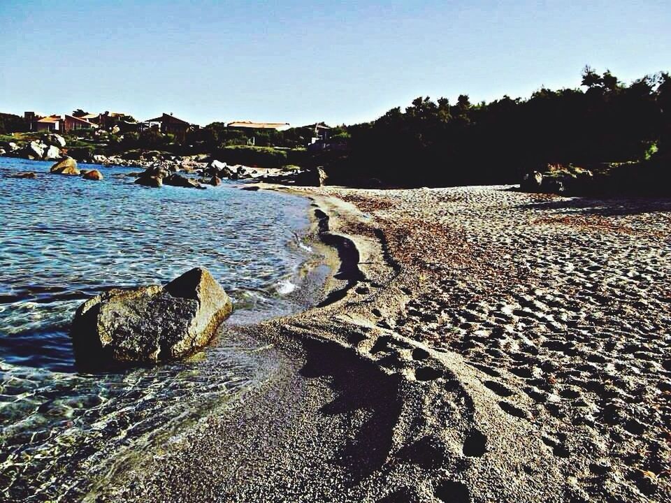 water, clear sky, beach, sea, tranquility, tranquil scene, shore, tree, scenics, transportation, nature, sand, blue, nautical vessel, rock - object, sky, incidental people, sunlight, copy space, mode of transport