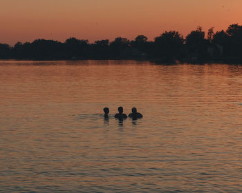 Silhouette man swimming in lake against sky during sunset