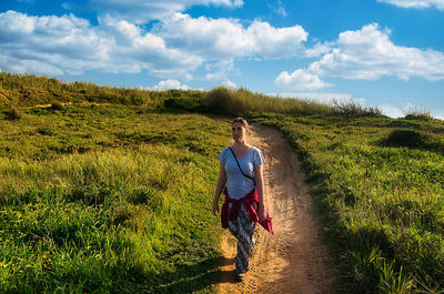 Rear view of woman walking on field against sky