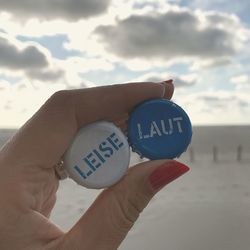 Close-up of hand holding text on sand at beach against sky