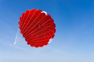 Low angle view of red parachute against clear blue sky