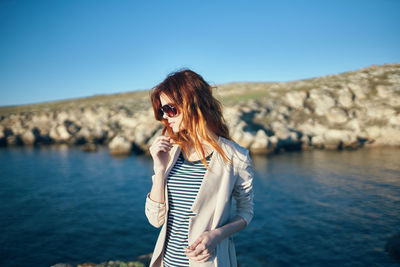 Young woman standing at shore against sky