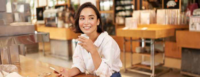 Portrait of young woman using mobile phone in cafe