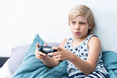 Boy holding joystick gaming controller in hands, playing video game at home.