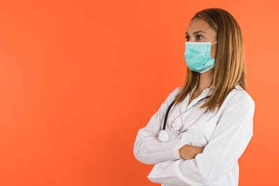 Portrait of female doctor holding medicine while standing against yellow background