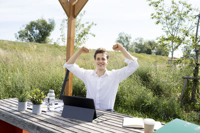 Rear view of man with arms raised standing against trees