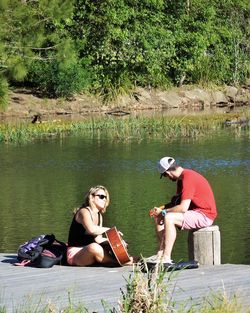 Women sitting by lake against trees