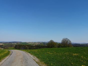 Empty road amidst field against clear blue sky