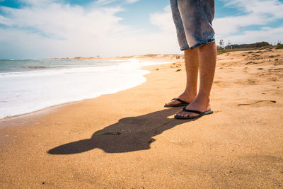 Low section of person standing on sand at beach