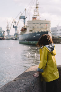 Woman traveler in raincoat admiring the icebreaker and cranes at shipyard. selective focus on girl