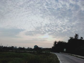 Road by trees against sky during sunset