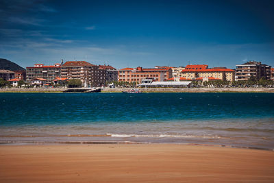 Scenic view of sea by buildings against blue sky