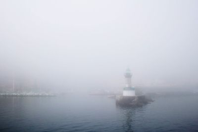 Lighthouse by sea during foggy weather