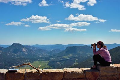 Side view of woman looking through binoculars while sitting on retaining wall