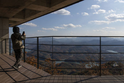 Woman photographing mountains with smart phone while standing in balcony