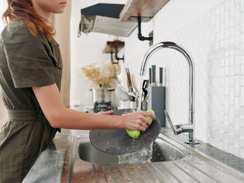 Midsection of woman washing hands in kitchen