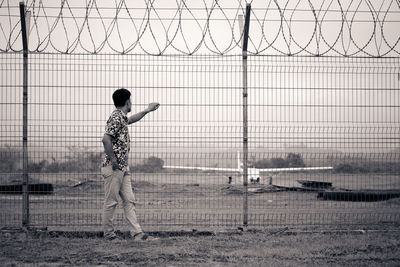 Side view of man standing by fence