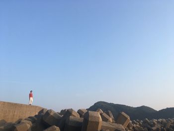 Man standing on rocks against clear blue sky