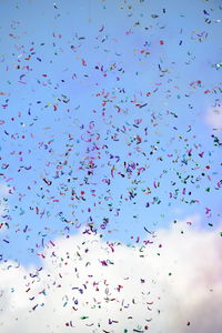 Low angle view of flock of birds flying against blue sky