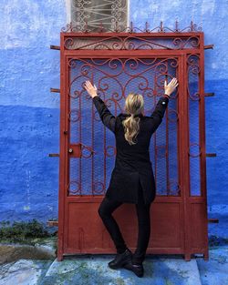 Rear view of woman touching metal gate against wall