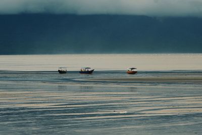 Boats sailing in sea against cloudy sky