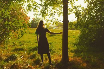 Rear view of young woman standing on grassy field at park