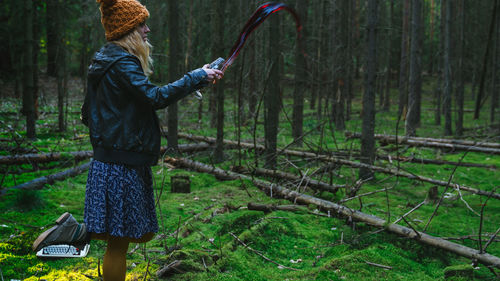 Girl in skirt and hat spilling red wine in mossy forest