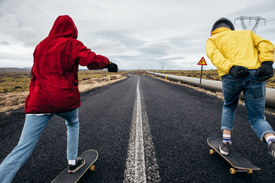 Full length of couple skateboarding on road against sky