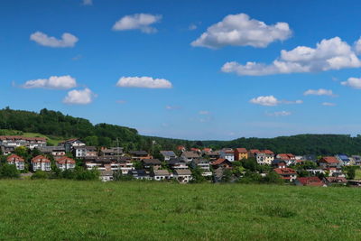 Houses on field by buildings against sky