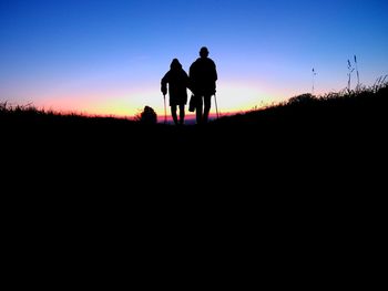 Rear view of silhouette men walking on road against sky