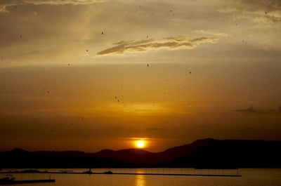 Scenic view of lake with jetty and boats by mountains at dusk