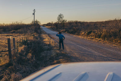 Rear view of man walking on road against clear sky