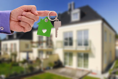 Cropped hand of man holding key ring against house