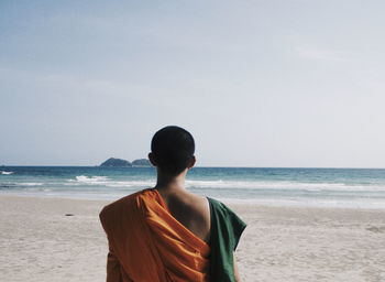 Rear view of monk standing on beach against clear sky