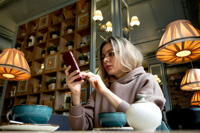 Caucasian middle-aged blonde woman sits in a cafe, drinks coffee and talks on a mobile phone