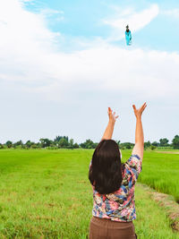 Rear view of woman with arms raised on field against sky