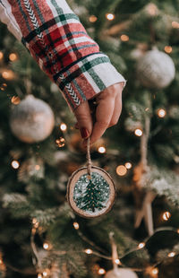 Female hand holding diy wooden handcrafted christmas ornament in front of christmas tree