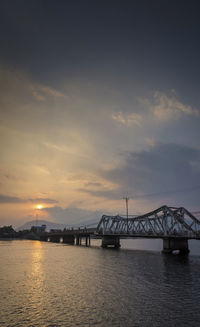 Silhouette bridge over sea against sky during sunset