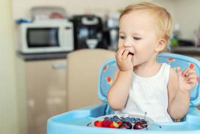 Close-up of cute baby boy eating cherry sitting at home