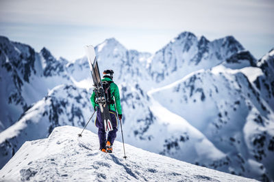 Man hiking on snowcapped mountain peak while looking at landscape against sky