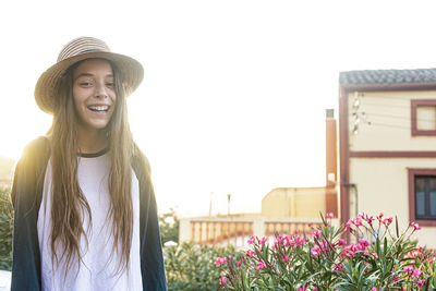 Smiling young woman wearing hat standing against building