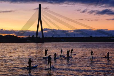 Silhouette people on sailboat at sea against sky during sunset