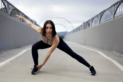 Portrait of woman exercising on bridge against sky