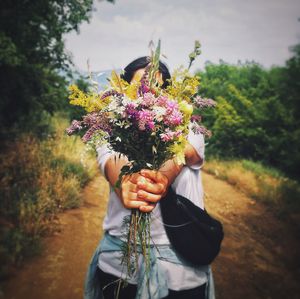 Low angle view of woman holding flowering plant on field