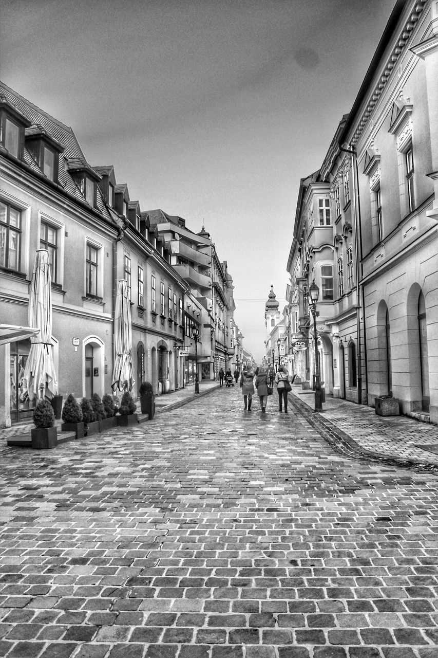 PEOPLE WALKING ON STREET AMIDST BUILDINGS AGAINST SKY